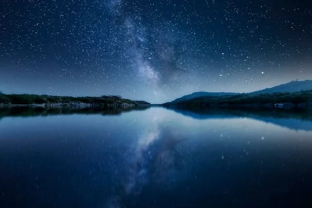 A breathtaking night photography shot of the Milky Way reflecting on a calm lake, with a star-filled sky above and serene natural landscapes in the background.