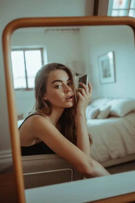 Aesthetic over-the-shoulder selfie pose taken in a cozy, neutral bedroom using natural light. Perfect for mirror selfies and Instagram content.