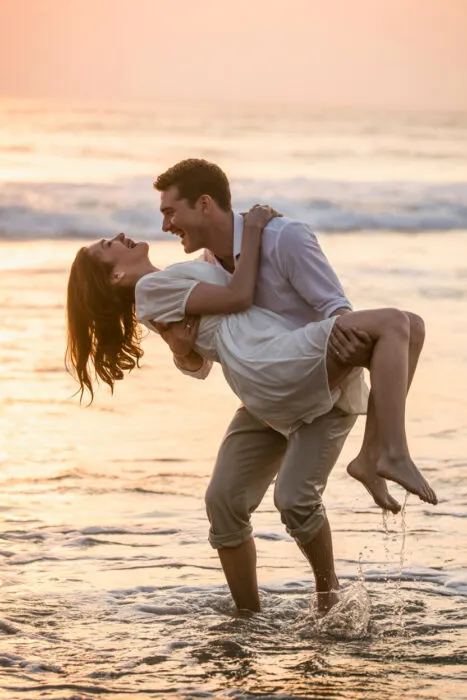 beach couple photography poses – lifting partner in the waves – fun & romantic beach photography idea.
