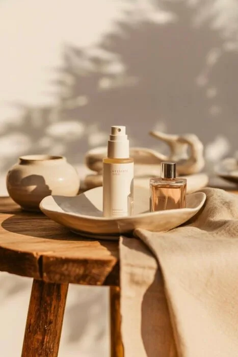 Elegant flat‑lay of skincare and fragrance bottles on a rustic wood table with soft beige linen and warm natural light, showcasing classy product photography style.