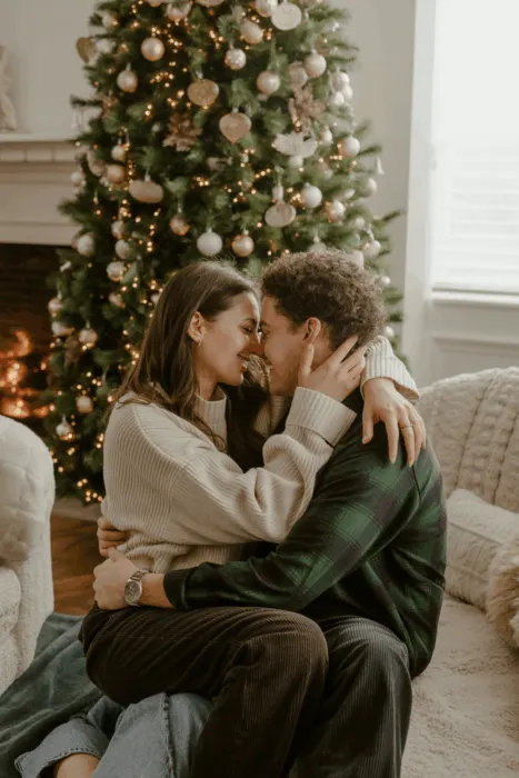 Romantic holiday couple taking cozy photos by the Christmas tree in festive outfits.