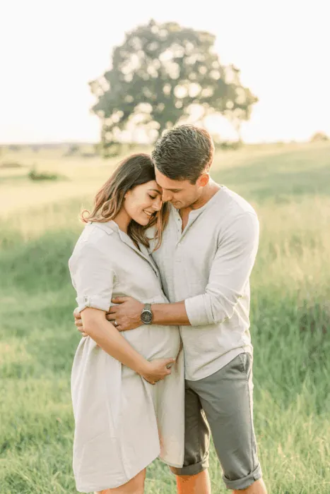 Candid maternity photo of a couple embracing outdoors in soft natural light with earthy color tones.