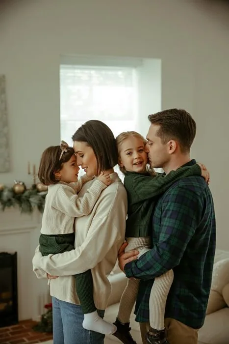 Family wearing coordinated Christmas outfits standing indoors with subtle holiday decor behind them.