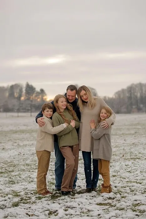 A family standing together outdoors in winter wearing neutral coats, sweaters, and jeans.