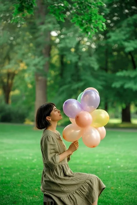 Woman sitting in a park holding balloons for a birthday photo.