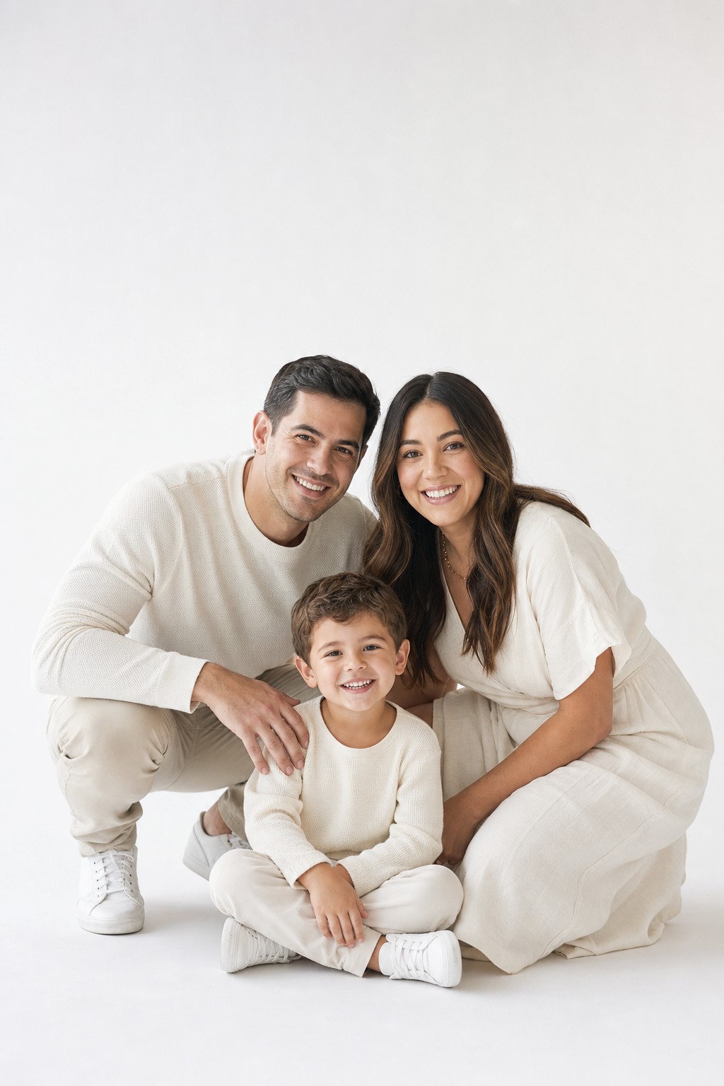 Family of 3 studio photo &mdash; parents and child in cream outfits against white backdrop
