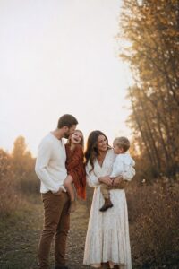 Family of four laughing together outdoors in golden hour light, fall family photo ideas pin