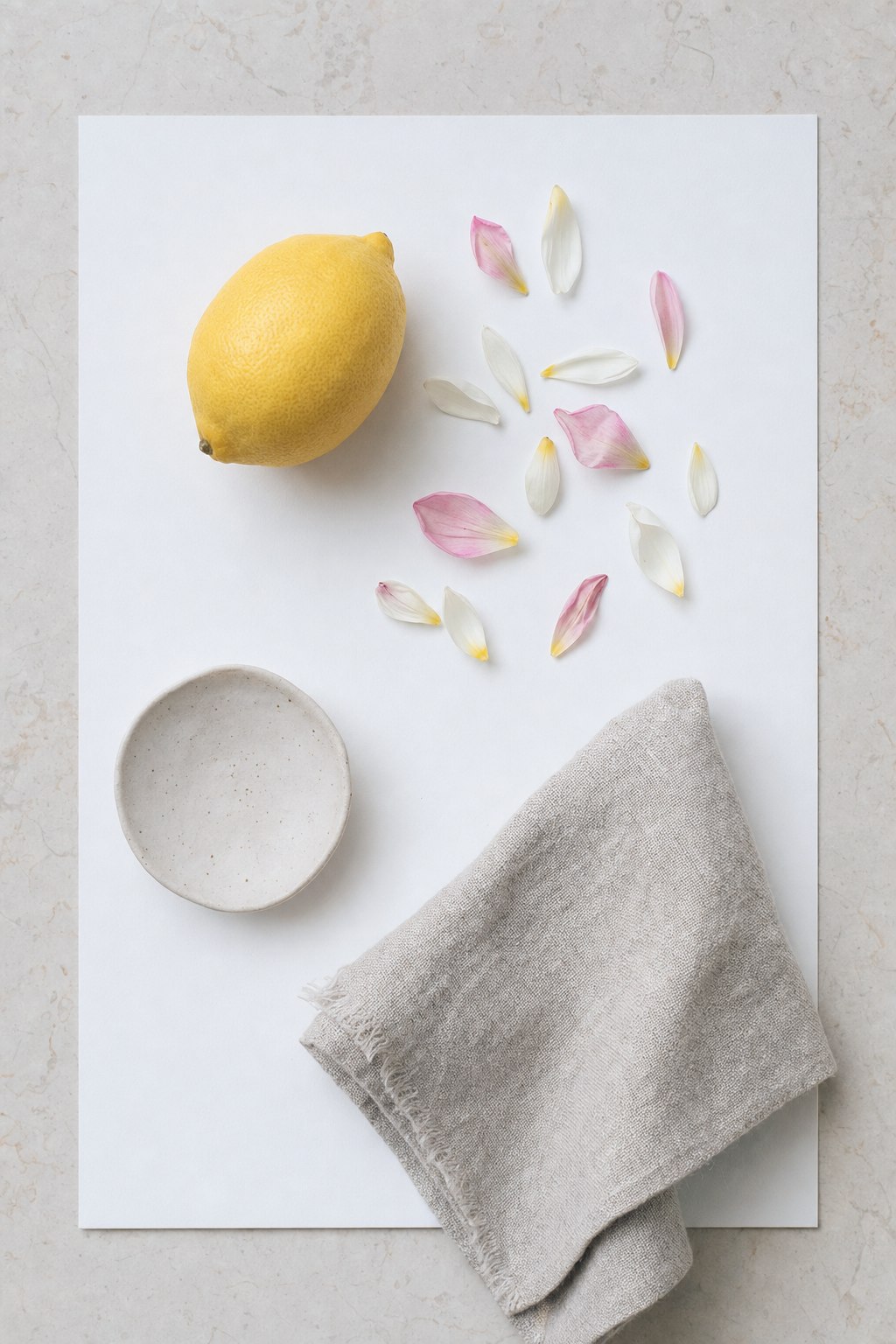 Overhead flat lay still life arrangement with lemon, petals, and ceramic on white card