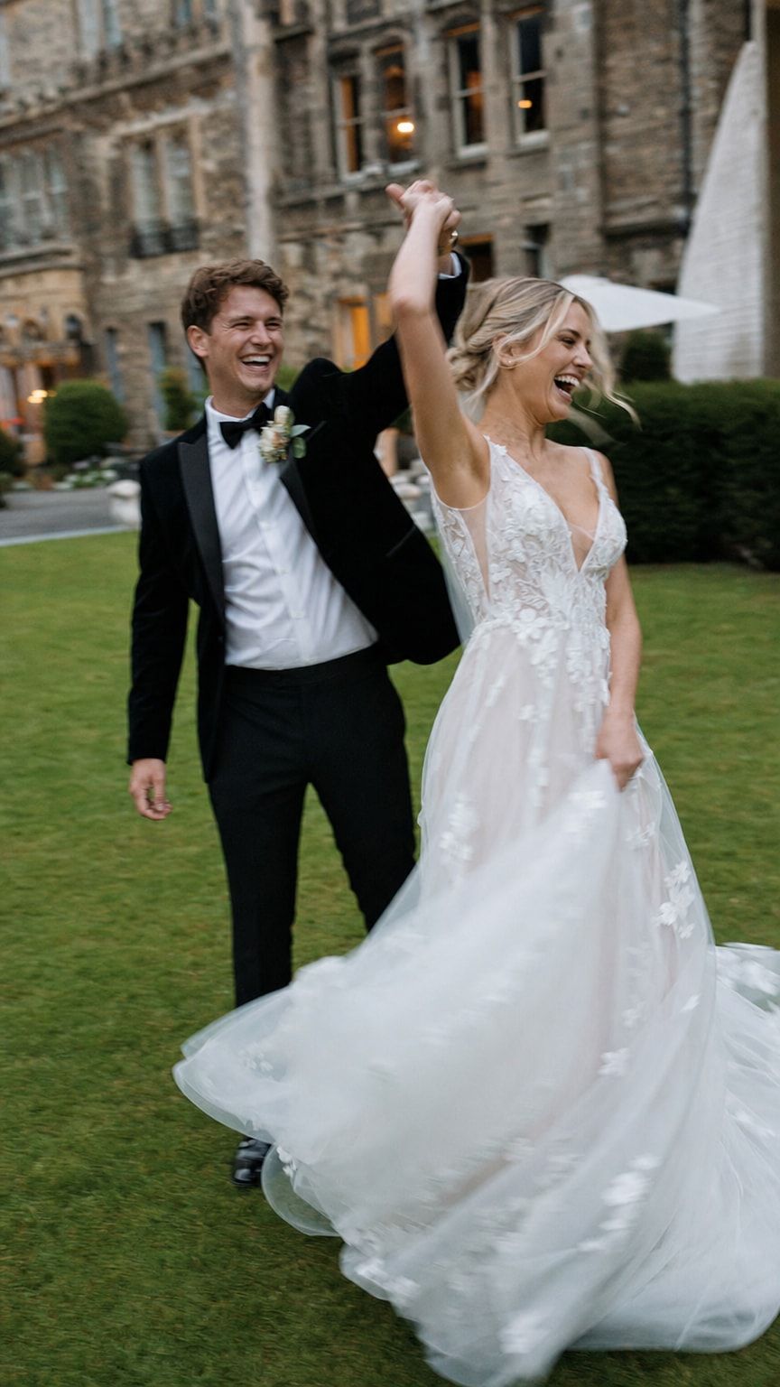 Wedding couple mid twirl on a lawn, dress fabric in motion, both laughing